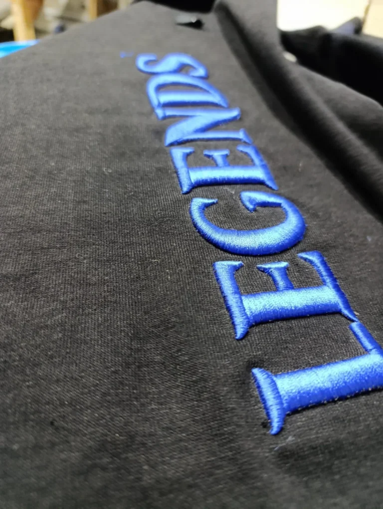 Close-up of blue 3D embroidered lettering on black fabric – made by Naxon Sports