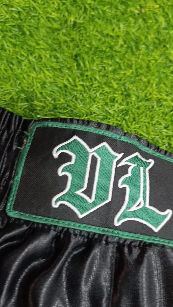 Traditional black satin Muay Thai shorts with stitched appliqué lettering, made at Naxon Sports factory in Sialkot