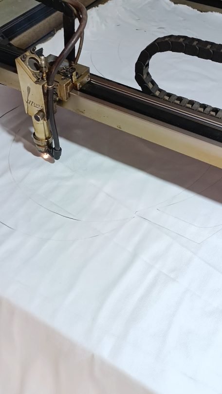Laser cutting machine cutting logo shapes from white fabric, following the design on the computer, at Naxon Sports factory in Sialkot