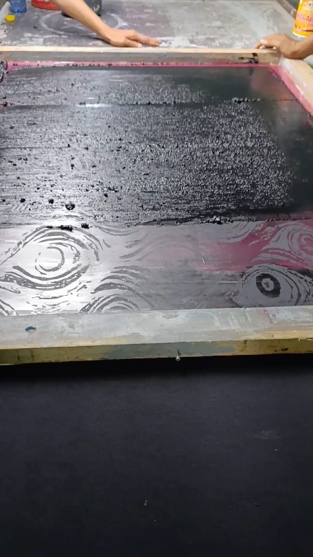 Screen printing ink pulled across a mesh screen onto black fabric at Naxon Sports factory in Sialkot