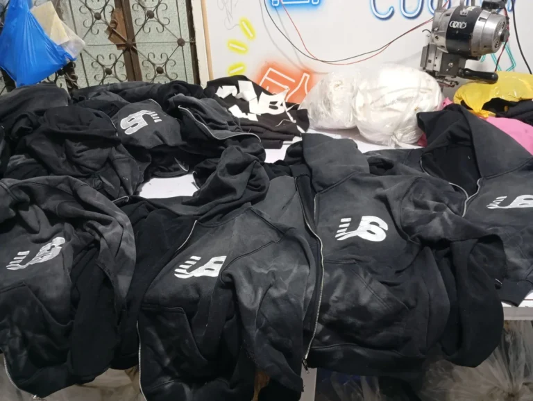 Stack of custom black jackets with printed logos in production – made by Naxon Sports