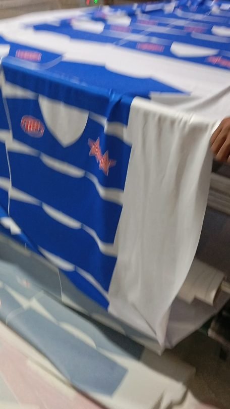 Worker taking blue and white striped sublimated jersey fabric off the heat press at Naxon Sports factory in Sialkot